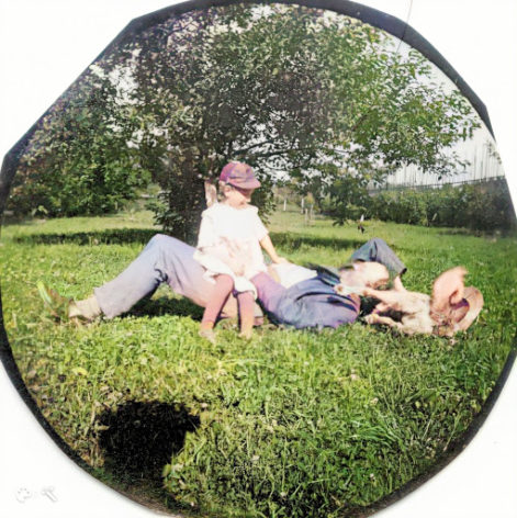 Dziecko z Ojcem, gdy ten leży w trawie i poklepuje ich psa, leżącego przy jego głowie